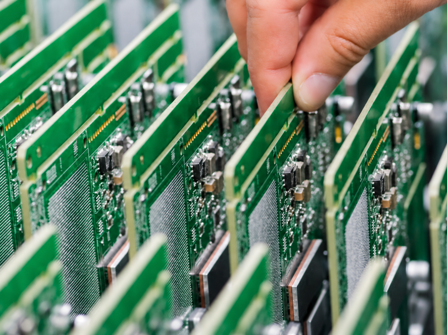 A hand selecting a green printed circuit board